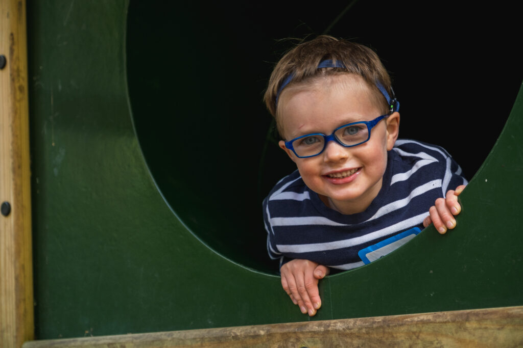 A smiling young boy with glasses at a playground