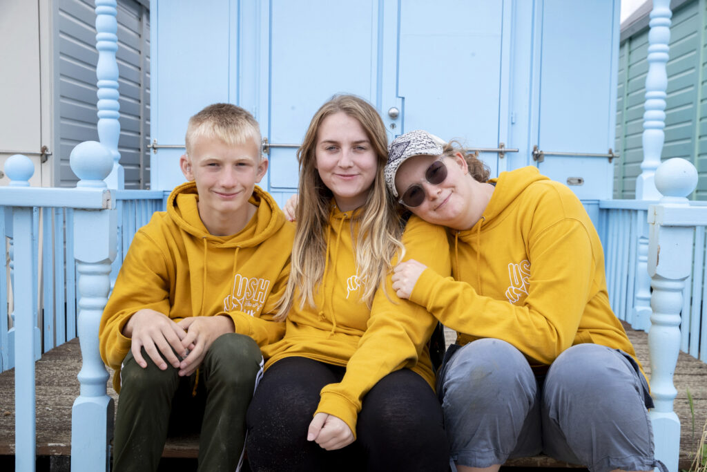 Three teenagers wearing yellow hoodies, sitting on a step
